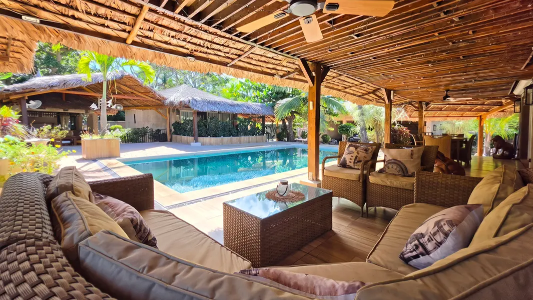 Terrasse couverte offrant un espace de réception avec vue sur la piscine et le jardin tropical.